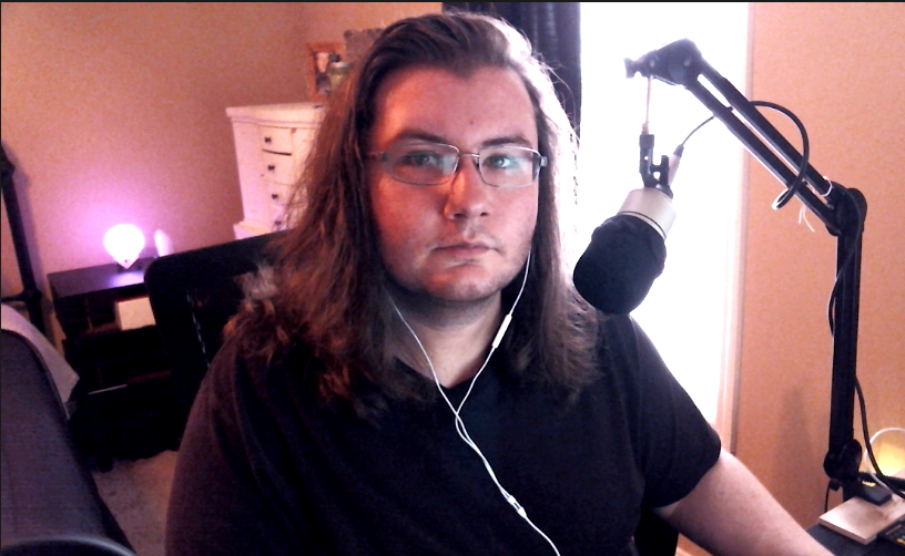 Dakota sitting at his desk, looking at the camera with a moon lamp behind him.